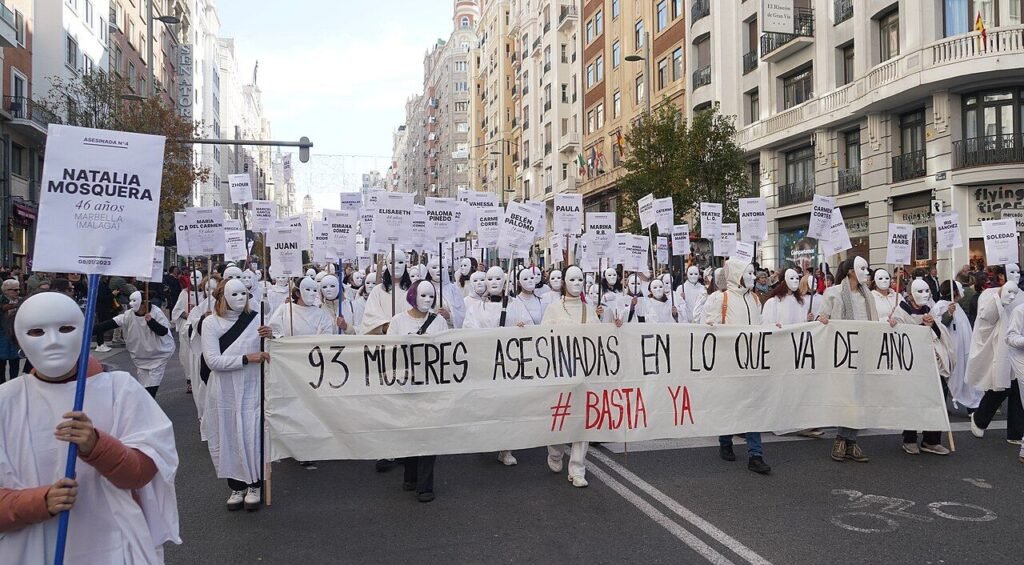 Mujeres vestidas de blanco con máscaras y carteles con el recuento de mujeres asesinadas en la manifestación del 25N en Madrid