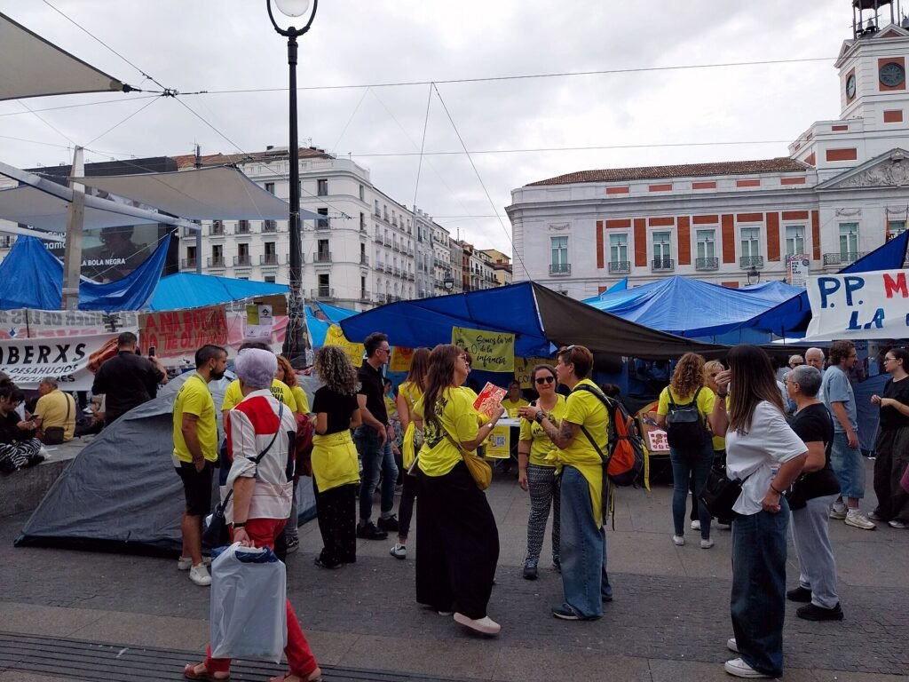 Personas con camisetas amarillas junto a las tiendas de la acampada por la vivienda en la Puerta del Sol