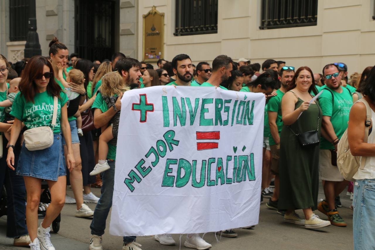 Manifestantes con un cartel blanco escrito a mano: «+ Inversión = Mejor educación»