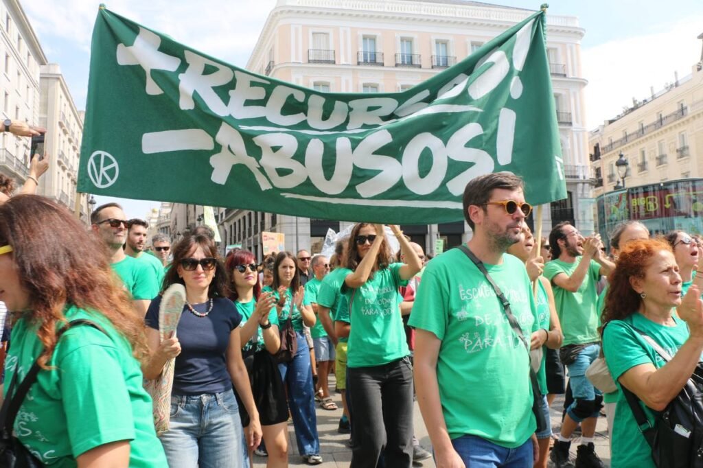 Docentes y familias con camisetas verdes bajo una gran pancarta «+Recursos! −Abusos!» en la manifestación por la educación pública