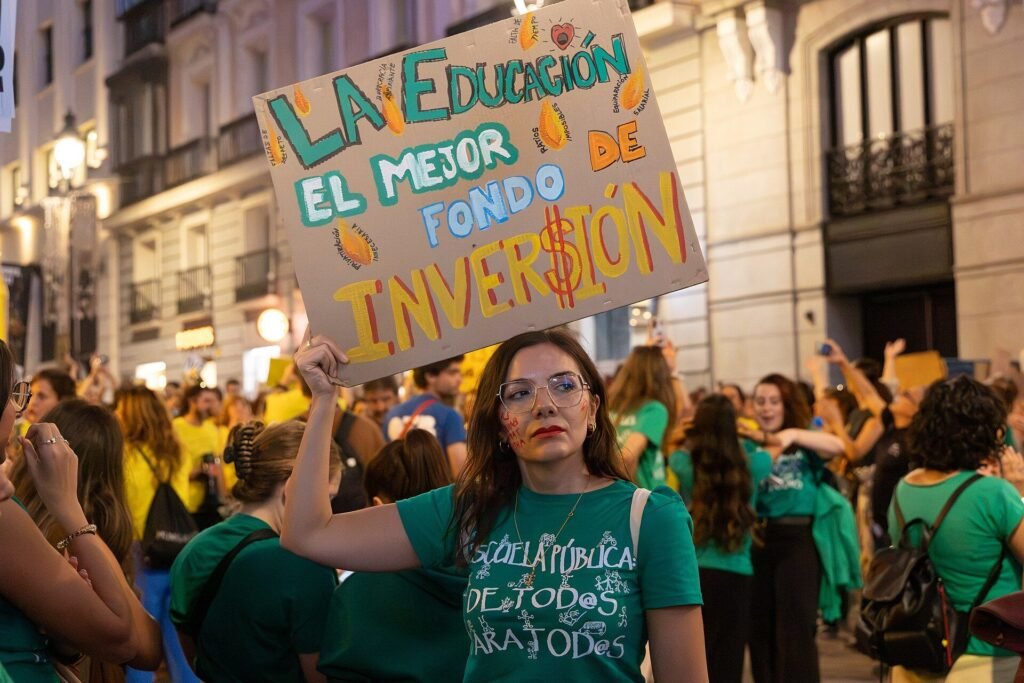 Una mujer con camiseta verde de la escuela pública sostiene un cartel en una manifestación por la educación pública en Madrid, octubre de 2026