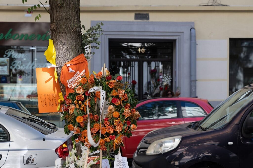 Corona de flores naranjas y una camiseta del Sindicato de Inquilinas en el memorial a Maricarmen en Sainz de Baranda